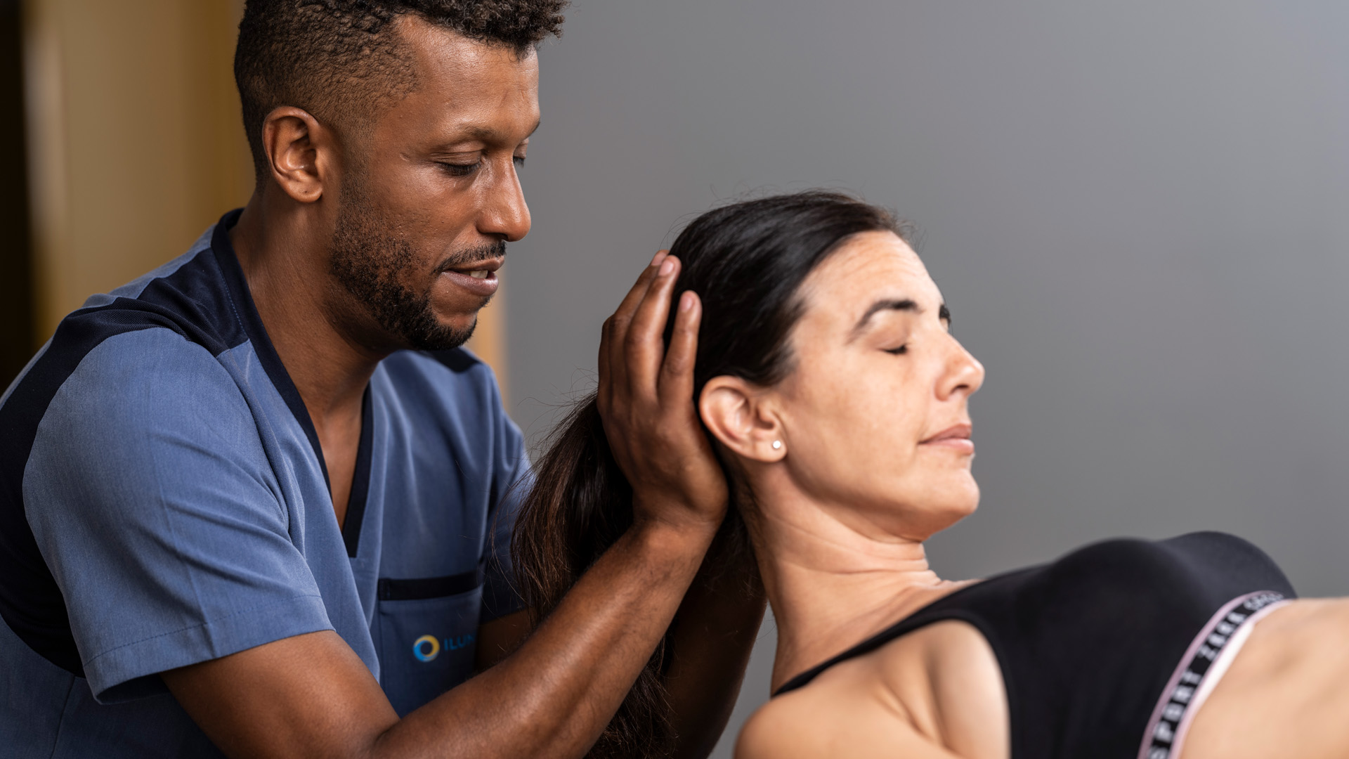 Profesional sanitario sostiene la cabeza y el cuello de una persona durante un ejercicio terapéutico en colchoneta.
